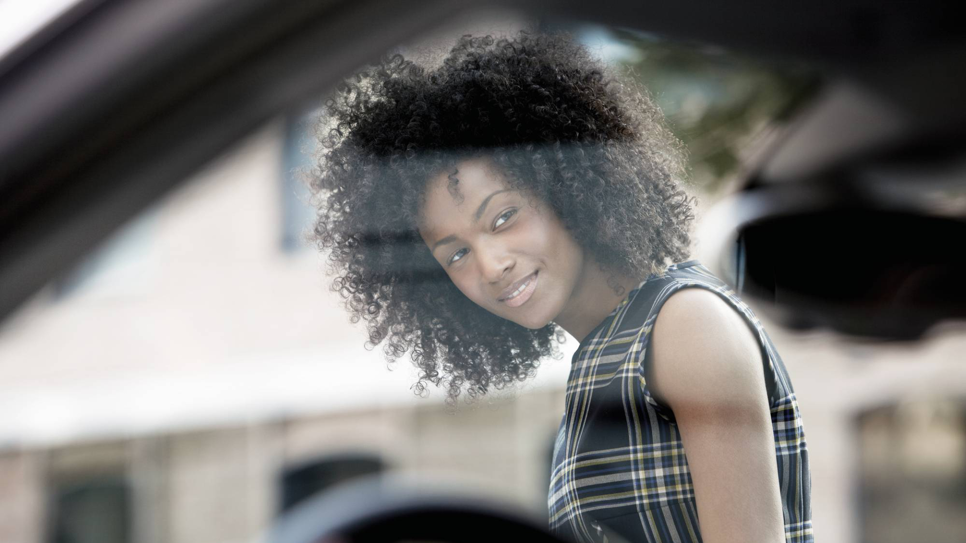 A woman stands next to an Audi and looks into the car with a curious but friendly expression.